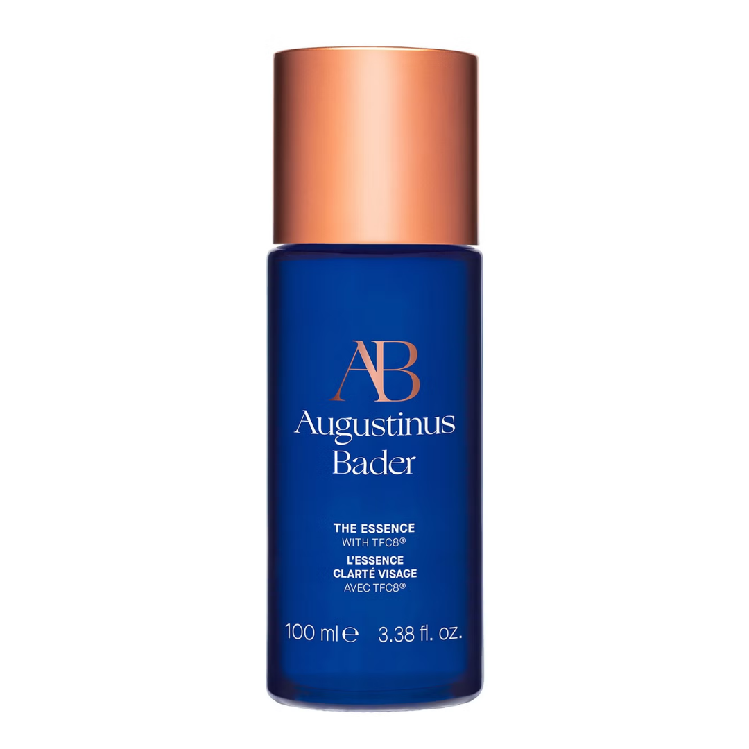 Augustinus Bader The Essence — tall cobalt blue bottle with copper cap, shown standing on a clean white surface.