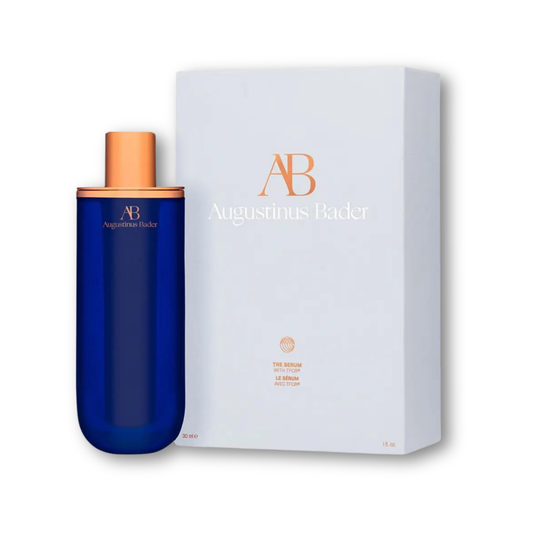 Augustinus Bader The Serum — slim cobalt blue bottle with copper pump dispenser, shown standing on a white surface.